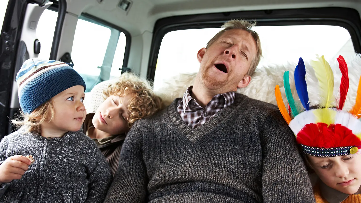 Ein Vater sitzt mit drei Kindern auf der Rückbank eines Autos und schläft