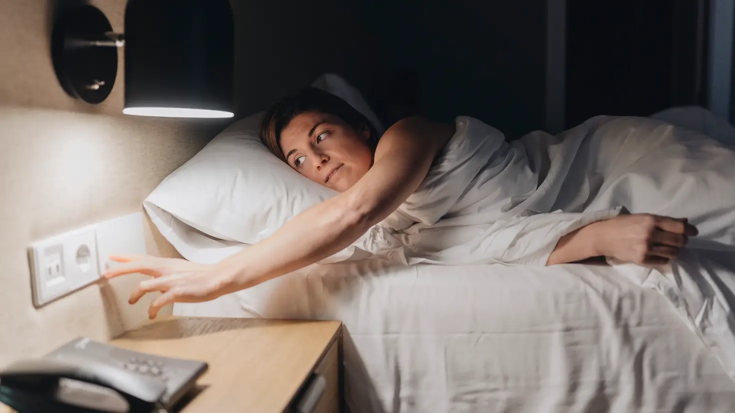Eine junge Frau liegt im Bett und schaltet das Licht aus