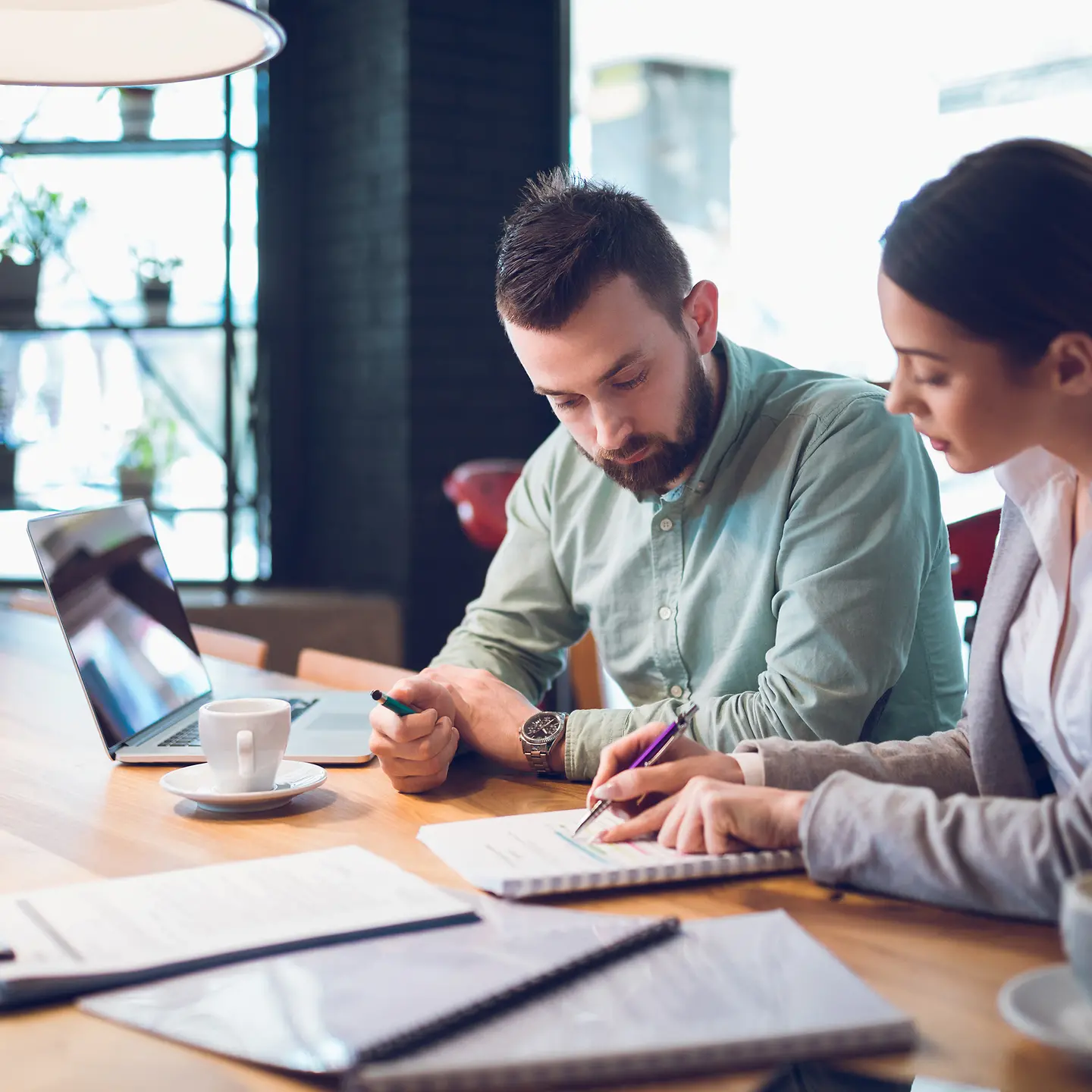 Zwei Geschäftspartner arbeiten im Büro mit Printmedien und Laptop an einem Projekt
