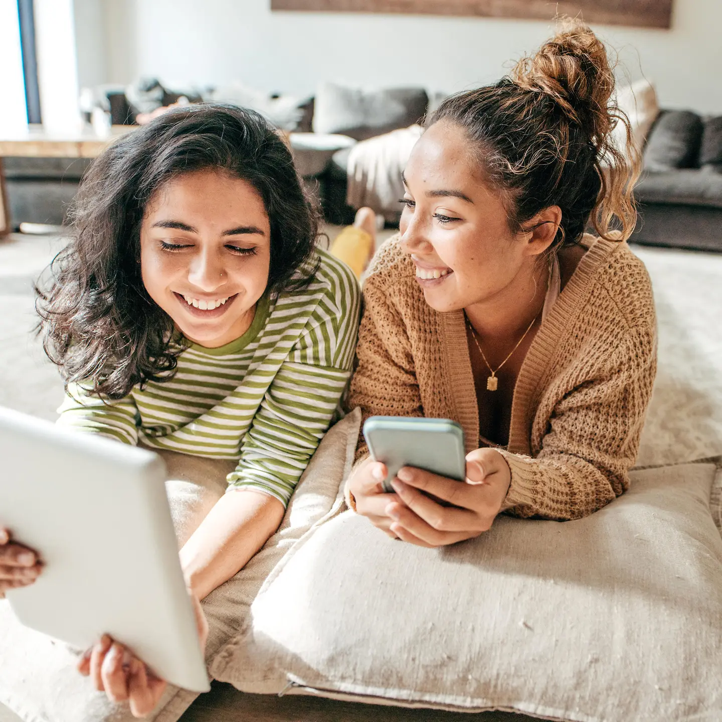 Zu sehen sind zwei Mädchen liegend mit Handy und Laptop