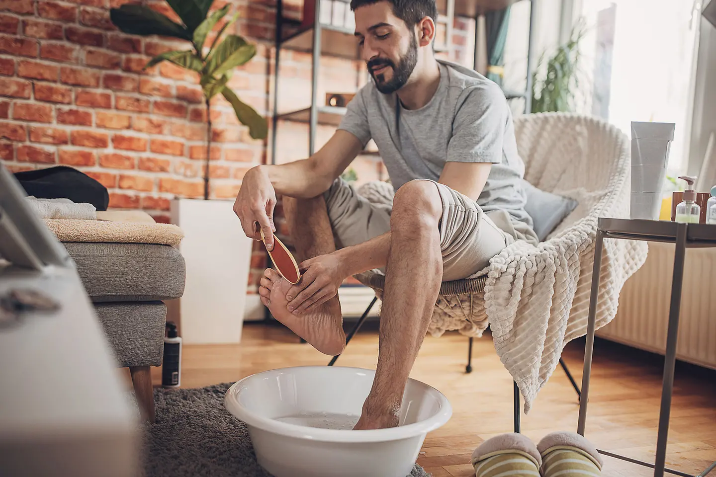 Zu sehen ist ein Mann der ein Fußbad macht und einen Fuß mit einem Bimsstein behandelt