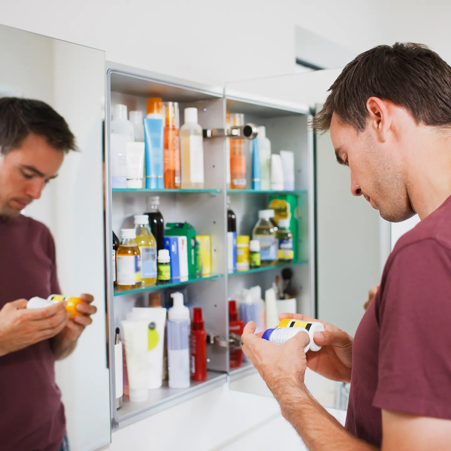 Ein Mann guckt skeptisch auf zwei Medikamentendosen im Badezimmer