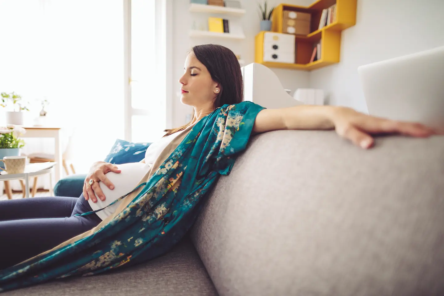 Schwangere Frau hält ihren Bauch und hat die Augen geschlossen_var