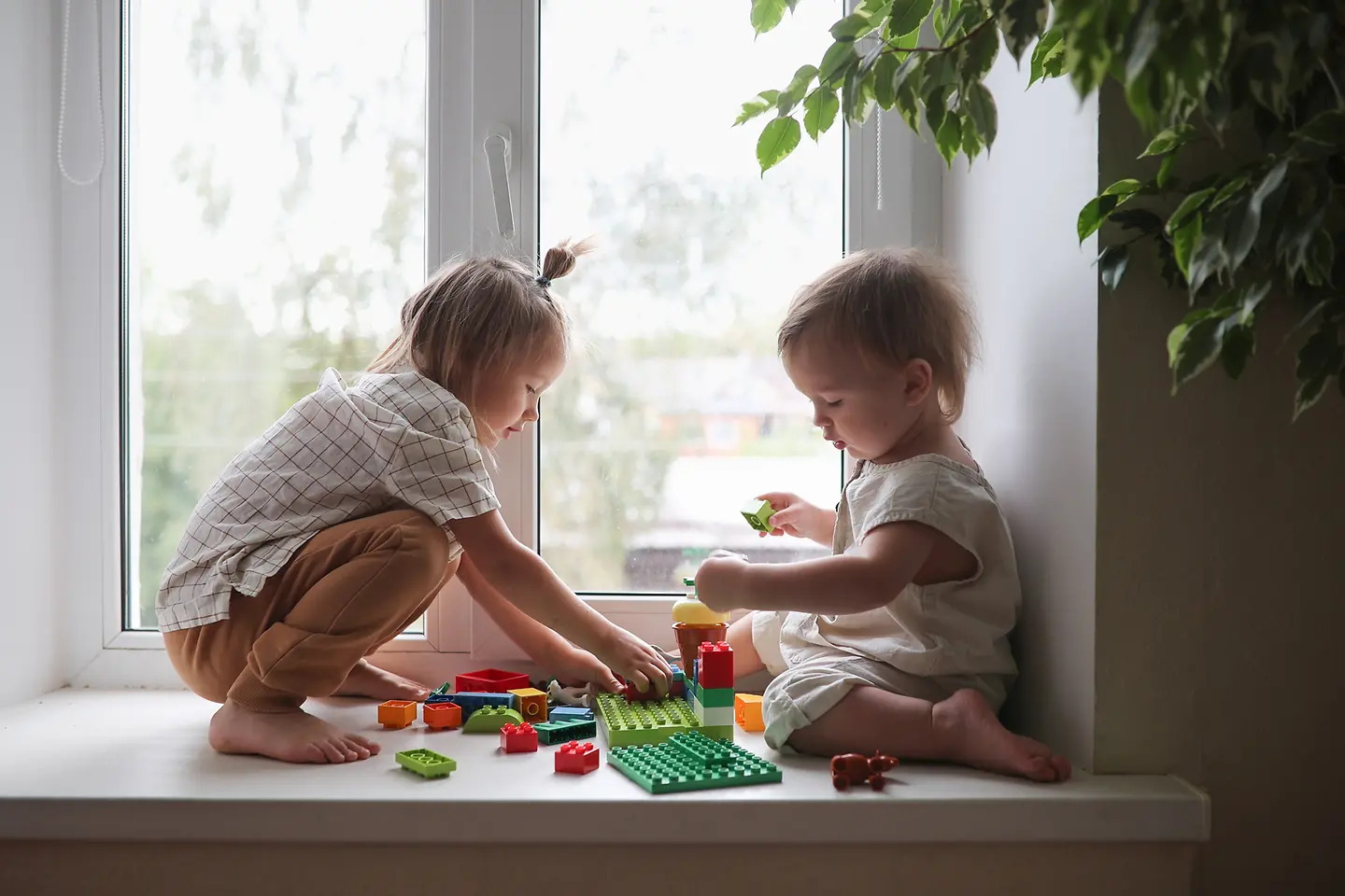 Zwei Kinder spielen auf einer Fensterbank mit Spielsteinen