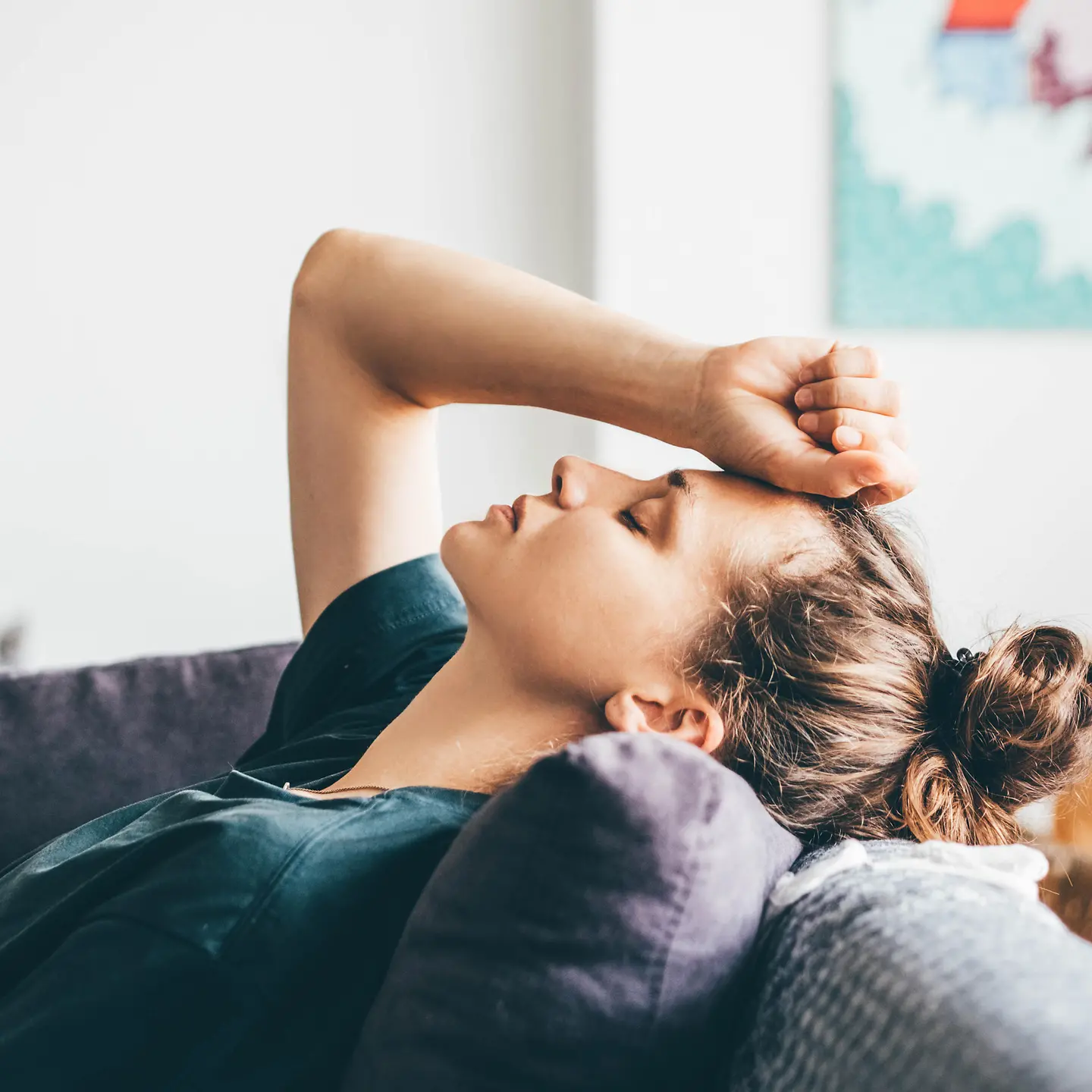 Eine junge Frau liegt mit Kopfschmerzen auf dem Sofa