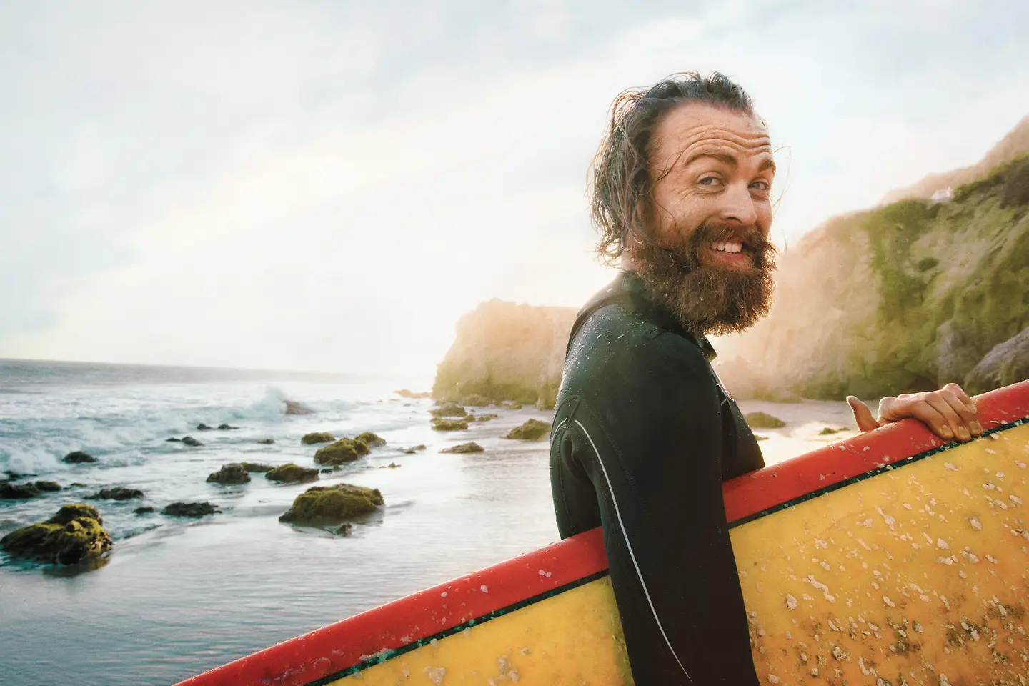 A man comes out of the sea carrying his surfboard