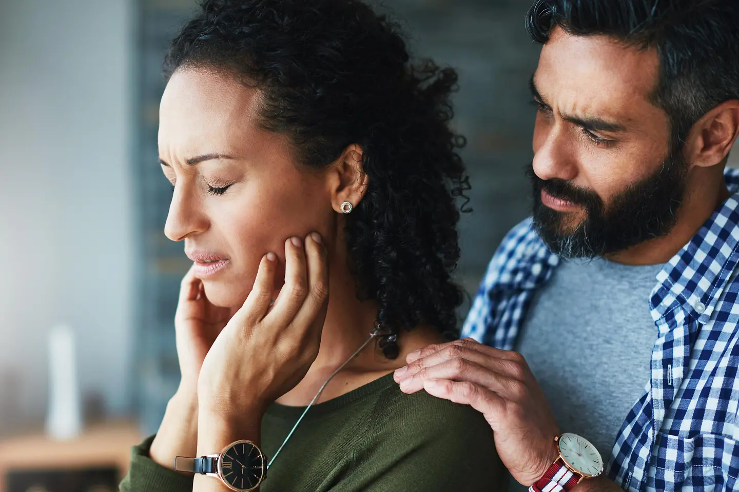 Eine Frau hält sich vor Schmerzen den Kiefer und ihr Mann steht besorgt hinter ihr