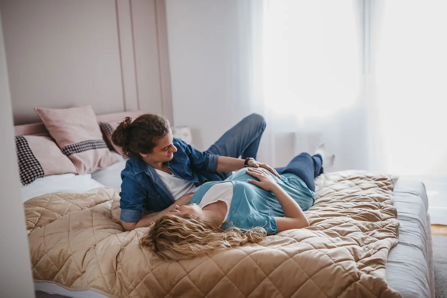 Junges Paar liegt auf einem Bett und streicheln den Babybauch der etwa 23. Schwangerschaftswoche