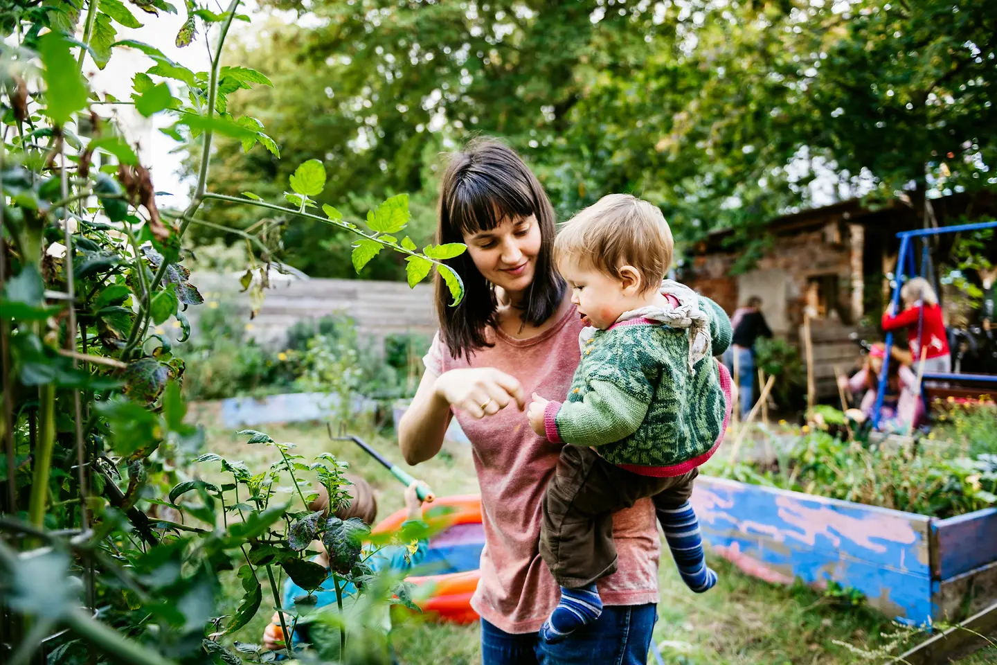 Mutter mit Kleinkind auf dem Arm isst frisch gepflückte Beeren im Garten 