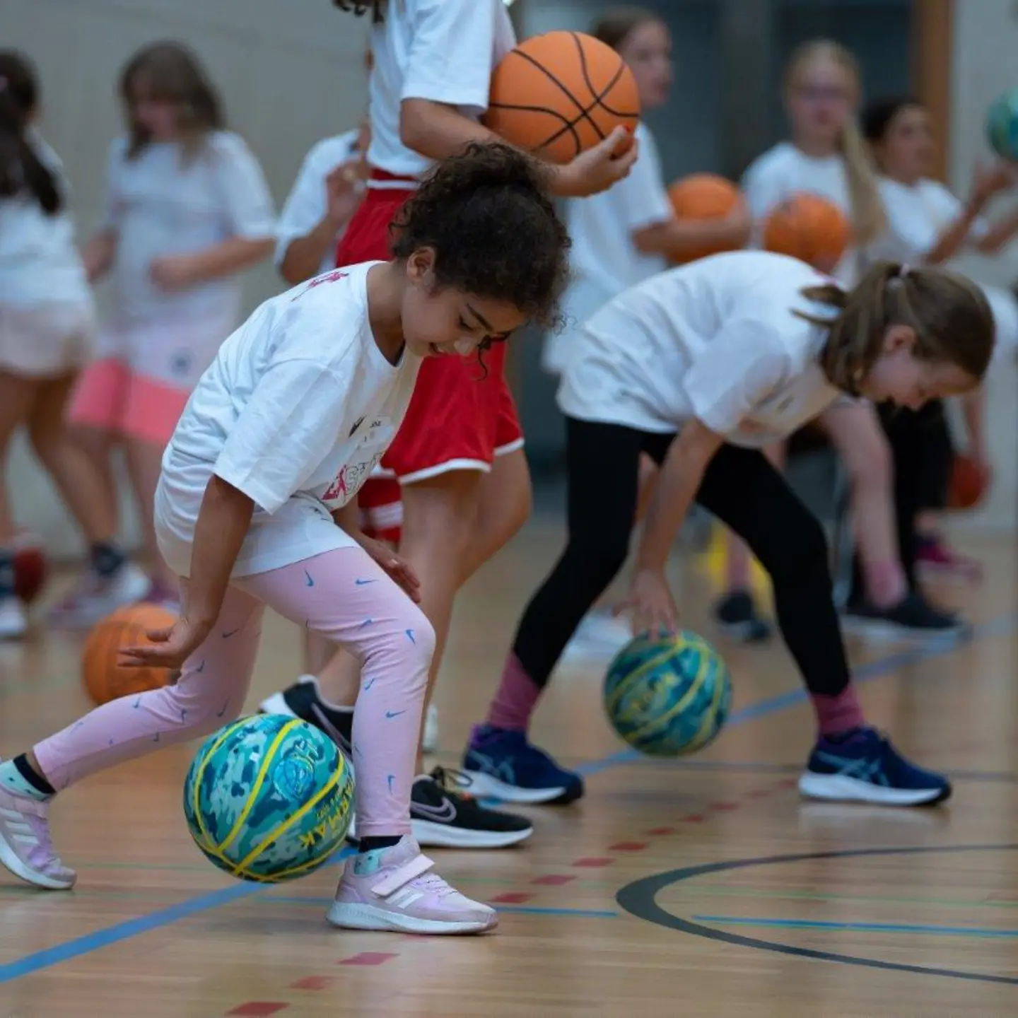 Zwei Mädchen spielen einen Ball durch ihre Beine, um das Dribbling zu üben.