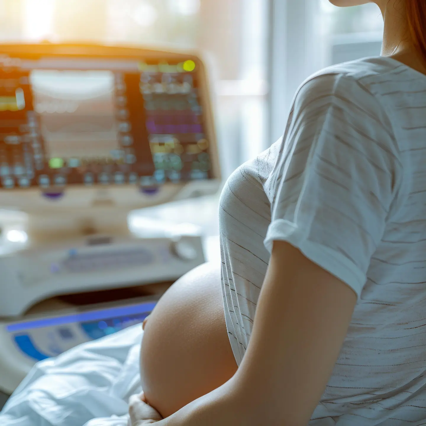 Zu sehen sind eine Schwangere Frau und ein Monitor, der verschiedene medizinische Kurven anzeigt