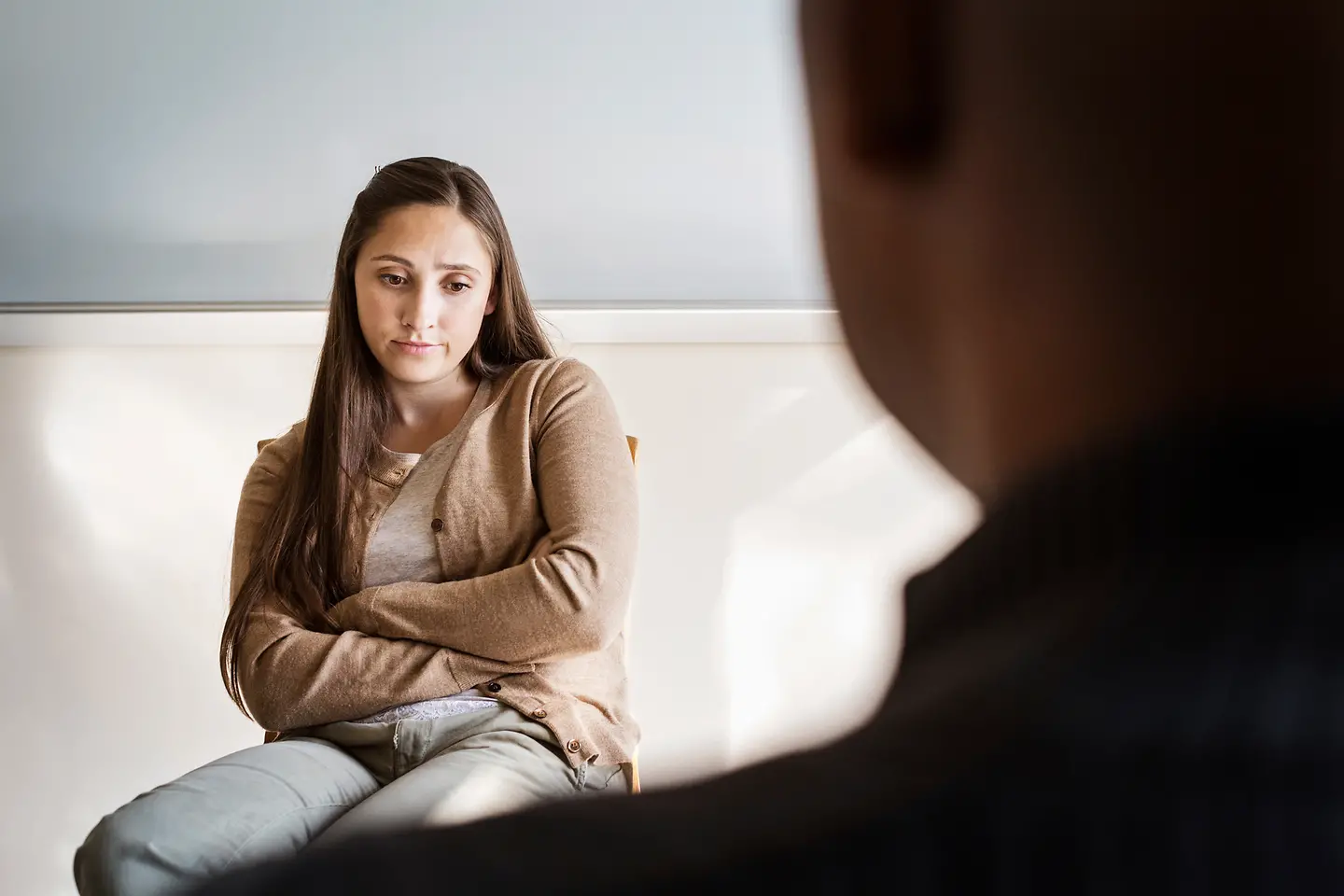 Eine junge Frau mit verschränkten Armen schaut traurig 