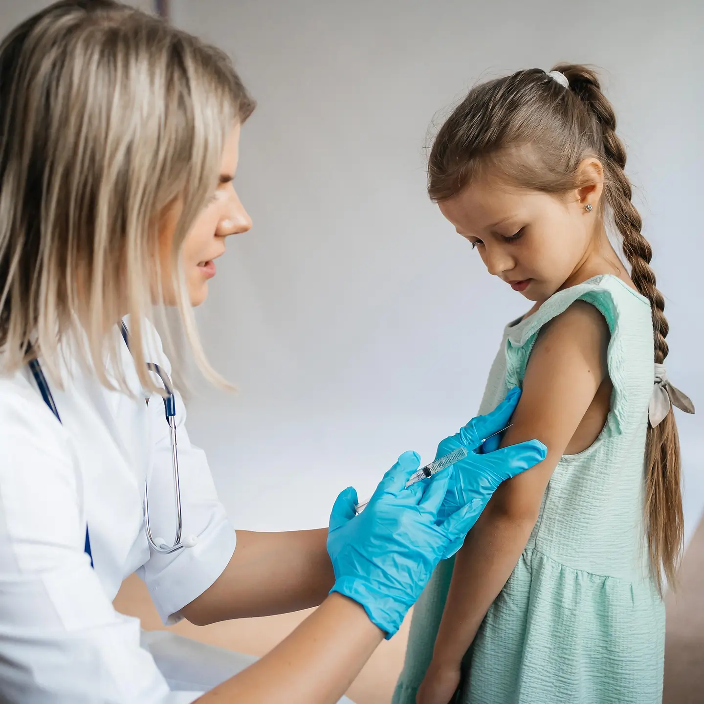 Eine Ärztin setzt eine Spritze mit einer Impfung beim Arm eines Mädchens an.