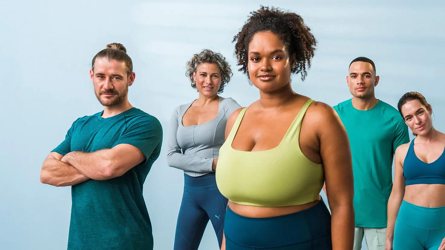 Eine Gruppe von sieben Menschen in Sportklamotten steht in einem Raum