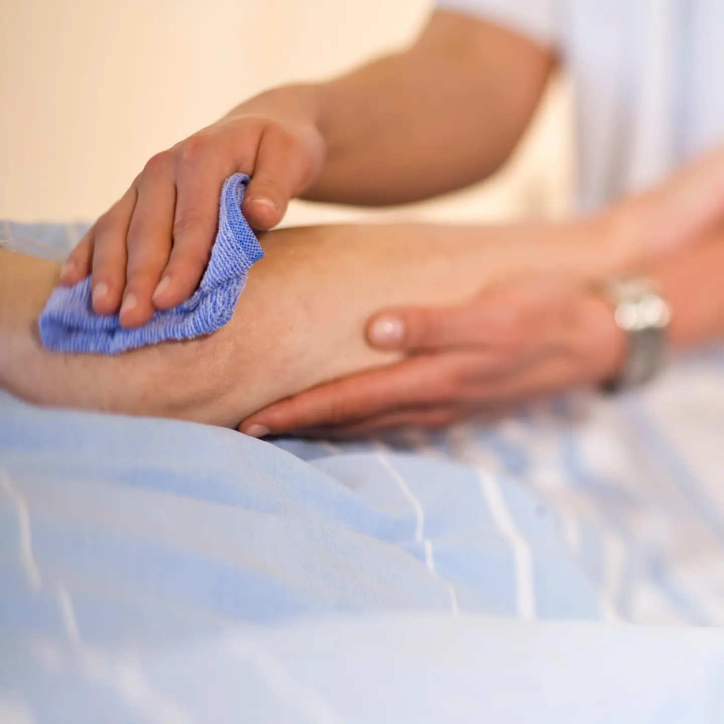Zu sehen sind zwei Hände, die mittels eines Lappens den Arm eines pflegebedürftigen Menschen waschen.