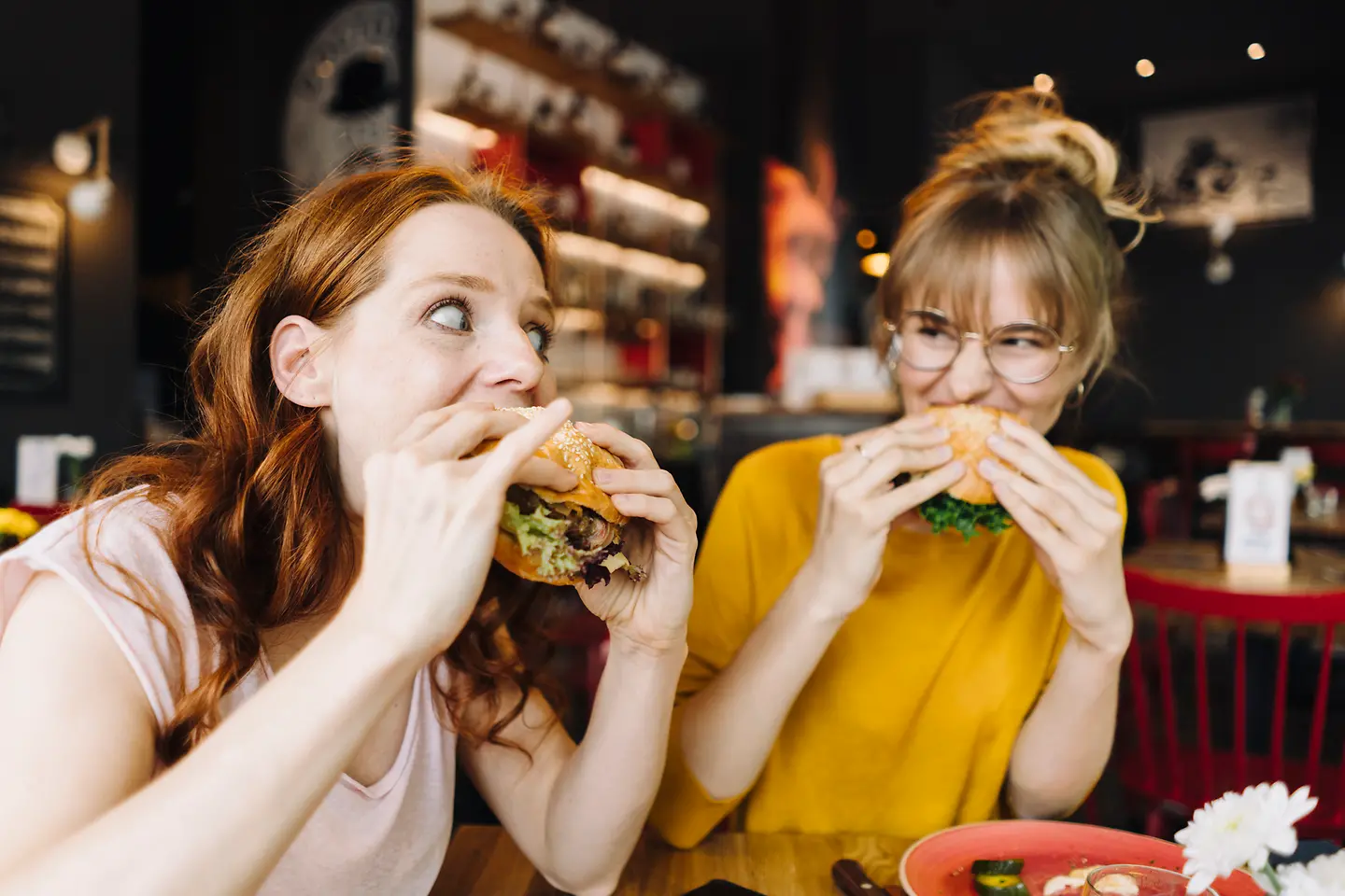 Zwei junge Frauen sitzen in einem Restaurant und essen genüsslich Burger