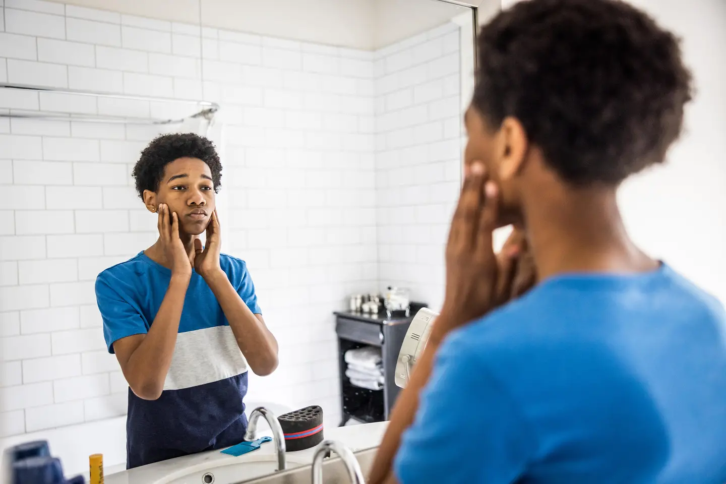 Ein schwarzer Teenager steht besorgt vor dem Badspiegel und fasst sich ins Gesicht