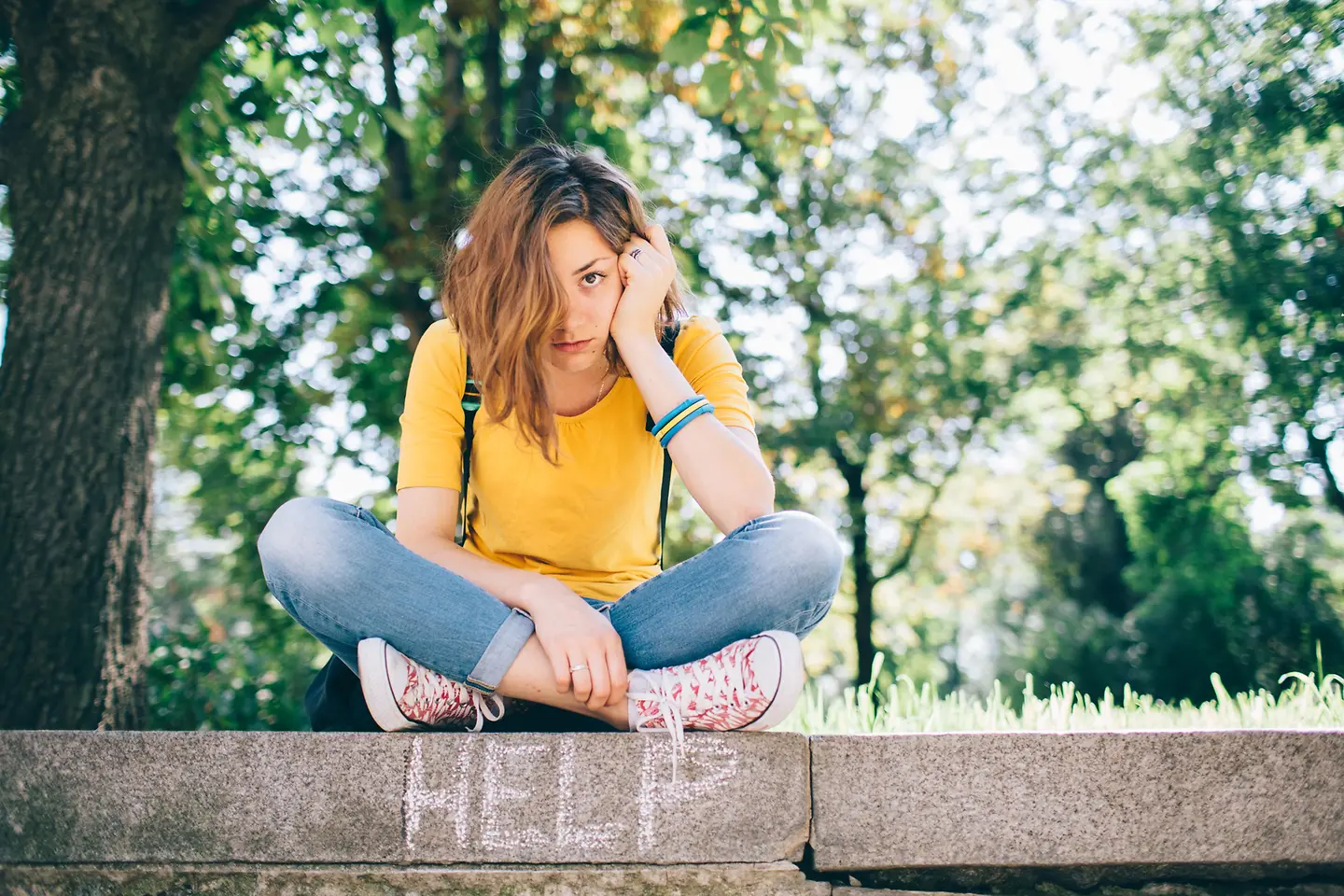 Junge erschöpfte Frau sitzt mit Rucksack auf einer Mauer. 