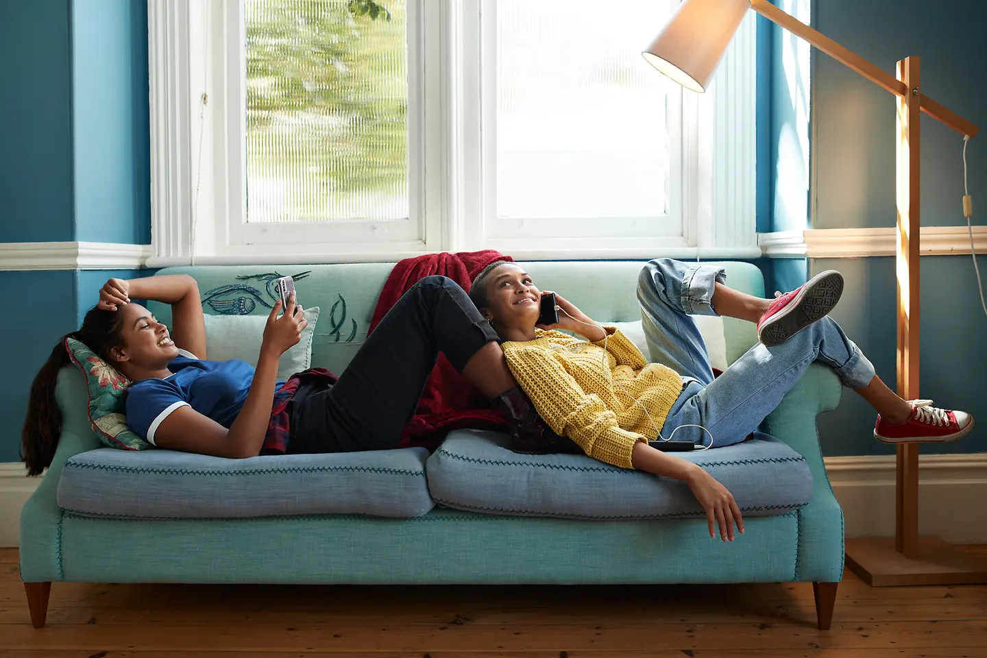 Lächelnde Freunde nutzen Handy während sie auf dem Sofa liegen