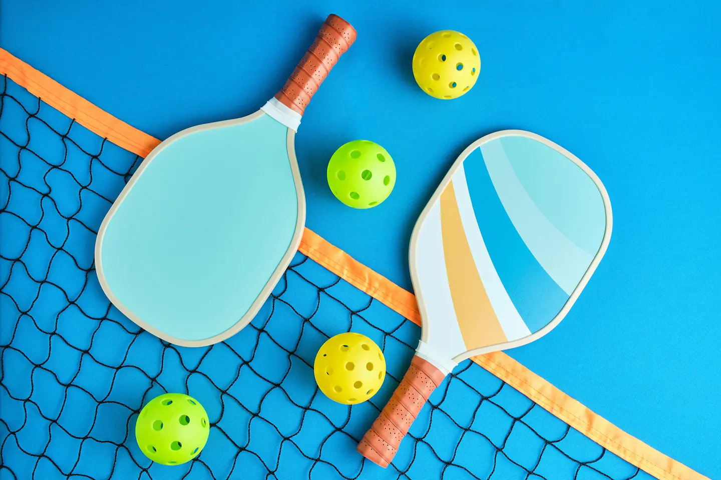 Zu sehen auf diesem Bild ist die Grundausstattung an Spielgerät für eine Partie Pickleball: zwei Paddel-Schläger, ein Netz und mehrere Spielbälle. 