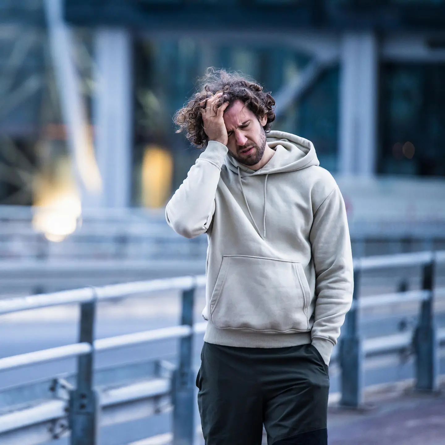 Sportlicher junger Mann mit Kopfschmerzen und Gehproblemen in der Stadt.