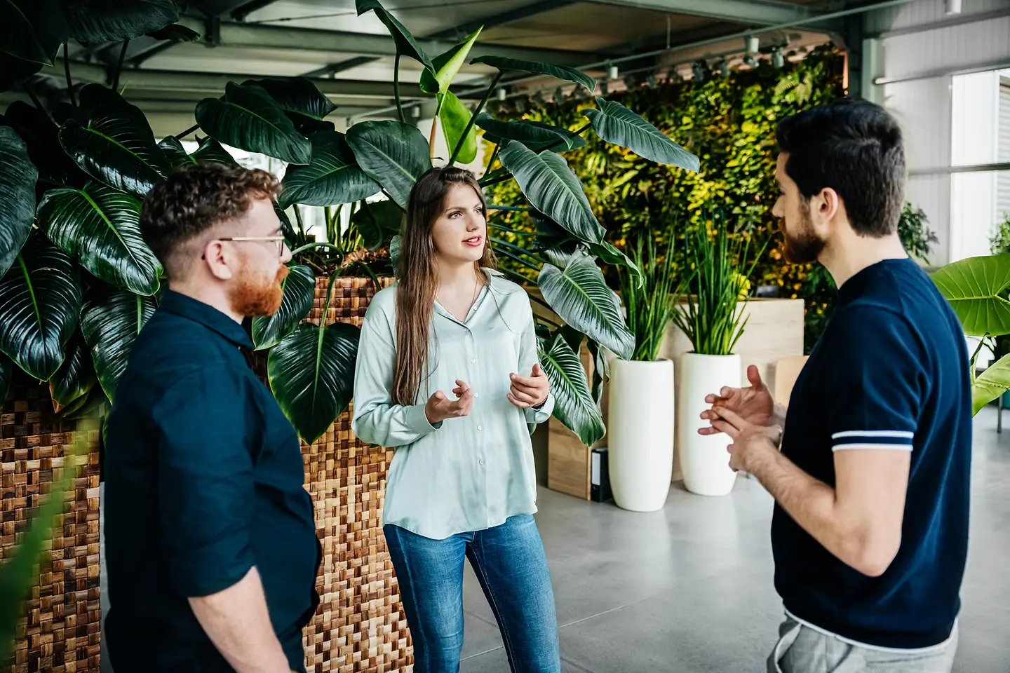 Drei junge Menschen unterhalten sich in einer Empfangshalle mit vielen Grünpflanzen
