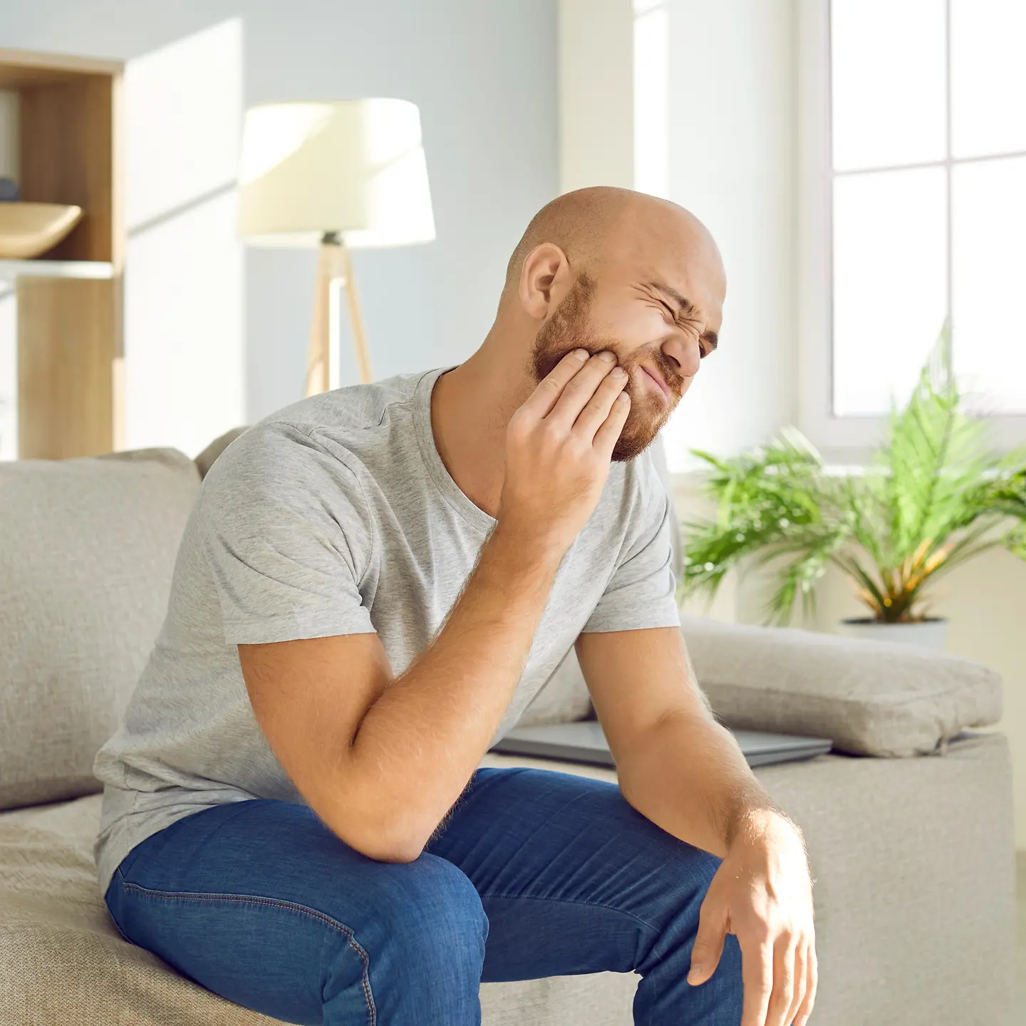 Junger Mann mit Zahnschmerzen zuhause auf dem Sofa