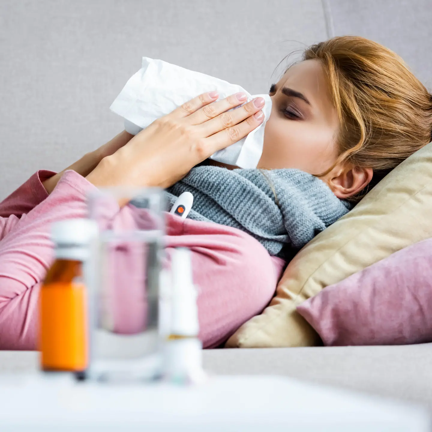 Eine Frau liegt mit Grippe im Bett und schnäuzt sich die Nase.