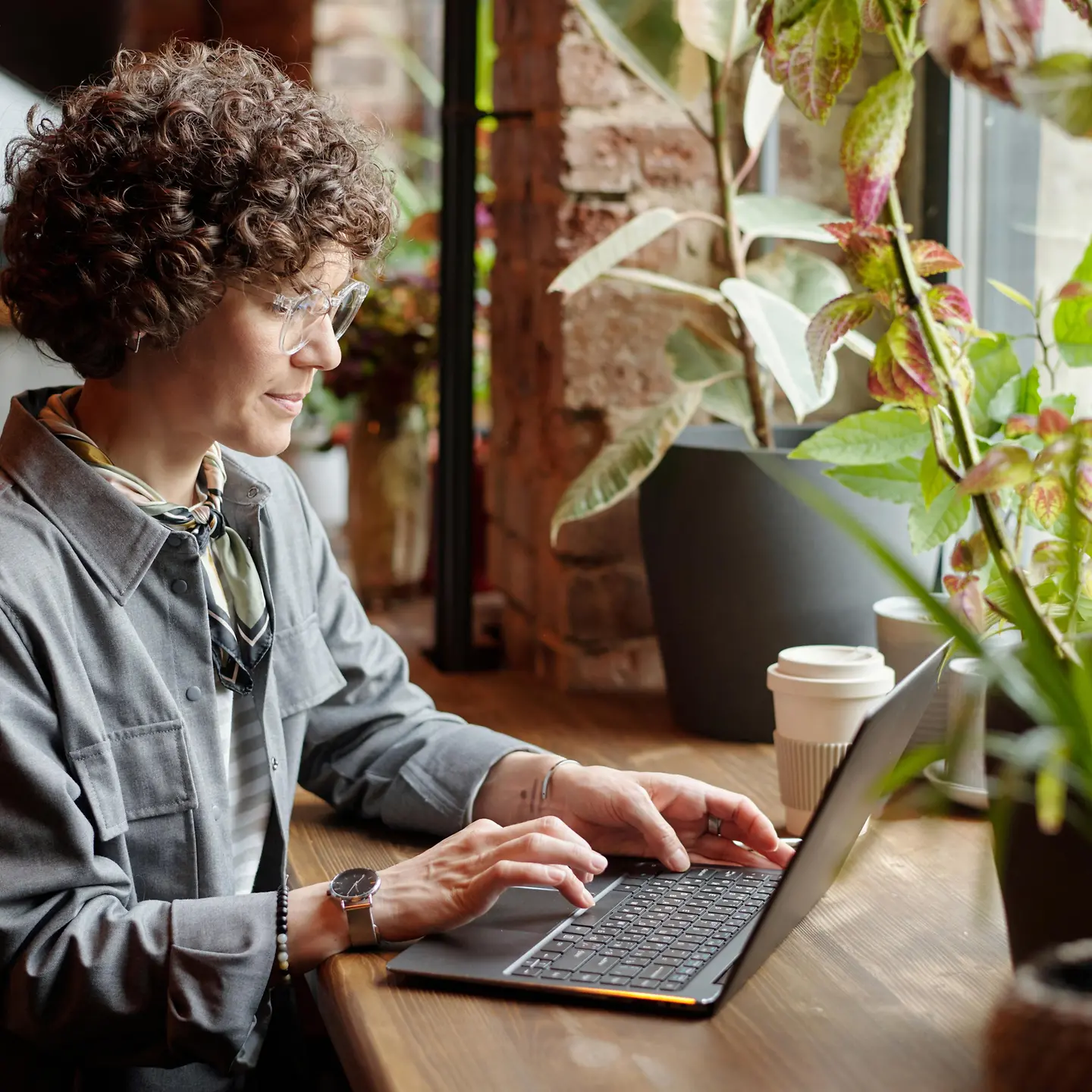Junge Frau sitzt mit ihrem Laptop an einem Fenster und arbeitet