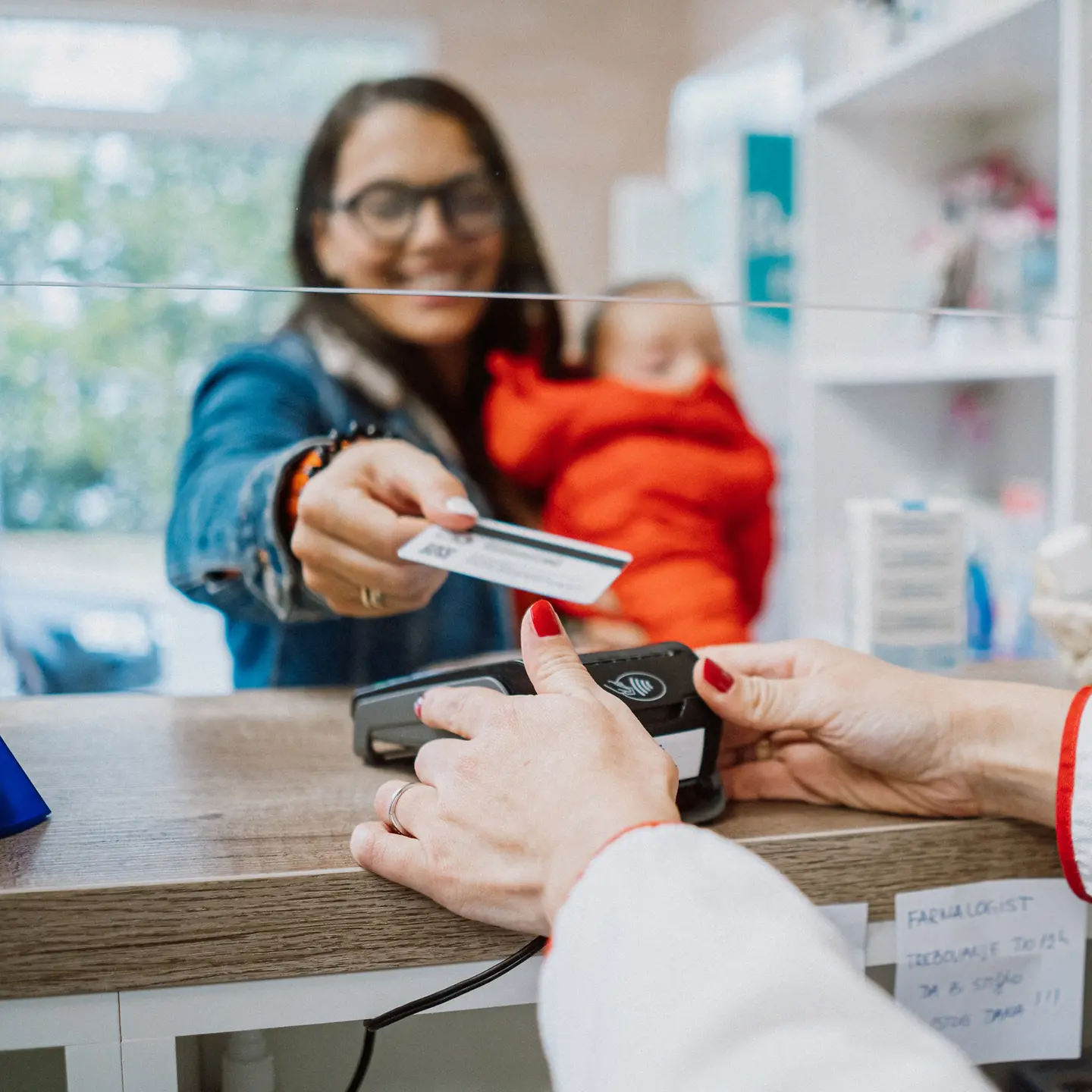 Eine Mutter, mit einer kleinen Tochter auf dem Arm, beim Einkauf in der Apotheke.