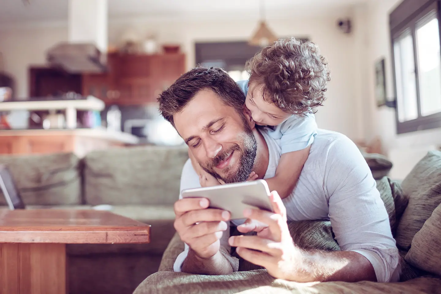 Ein Vater trägt seinen Sohn auf den Schultern und schaut auf sein Handy