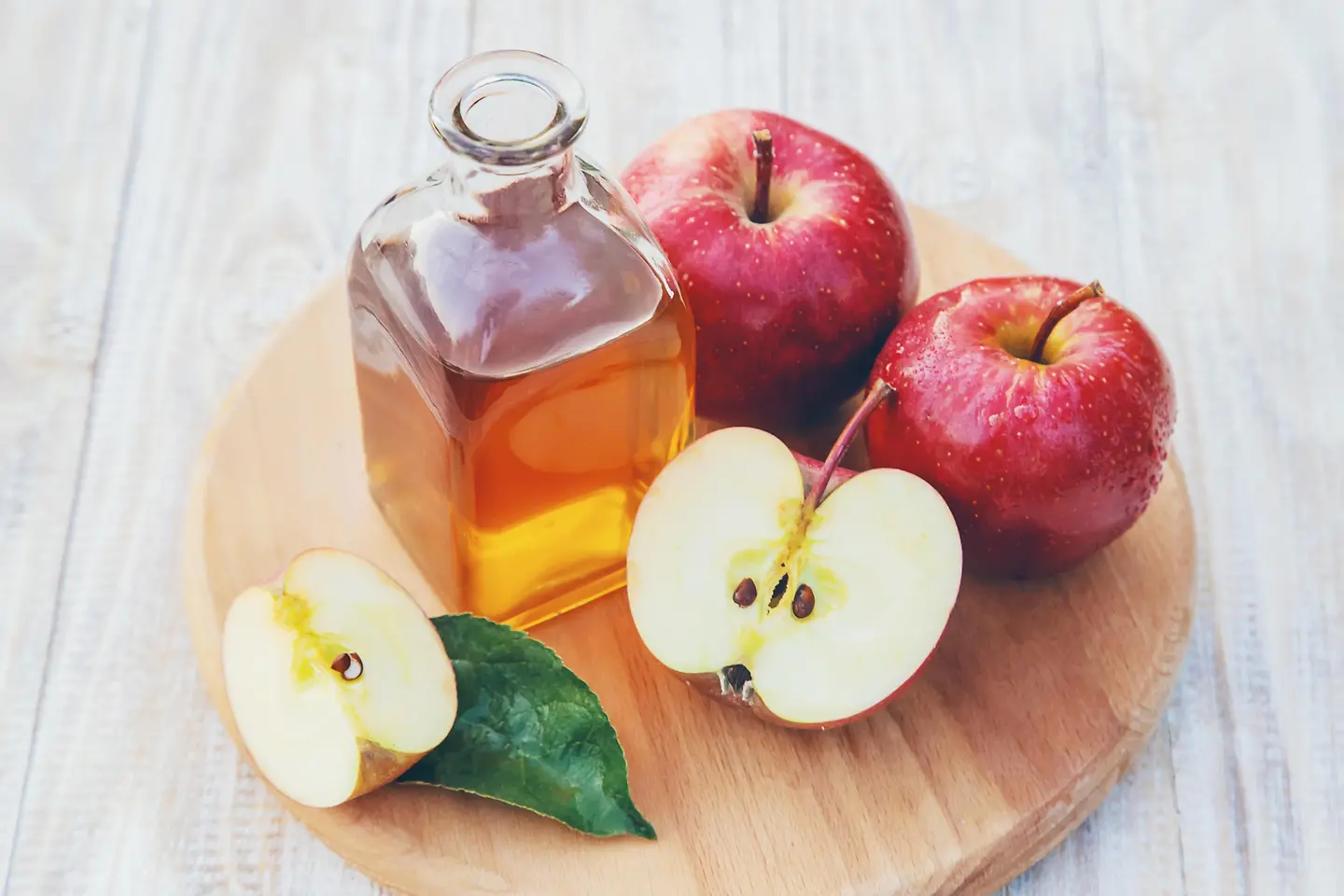 Apfelessig in einer Flasche und einige Äpfel auf einem Tisch
