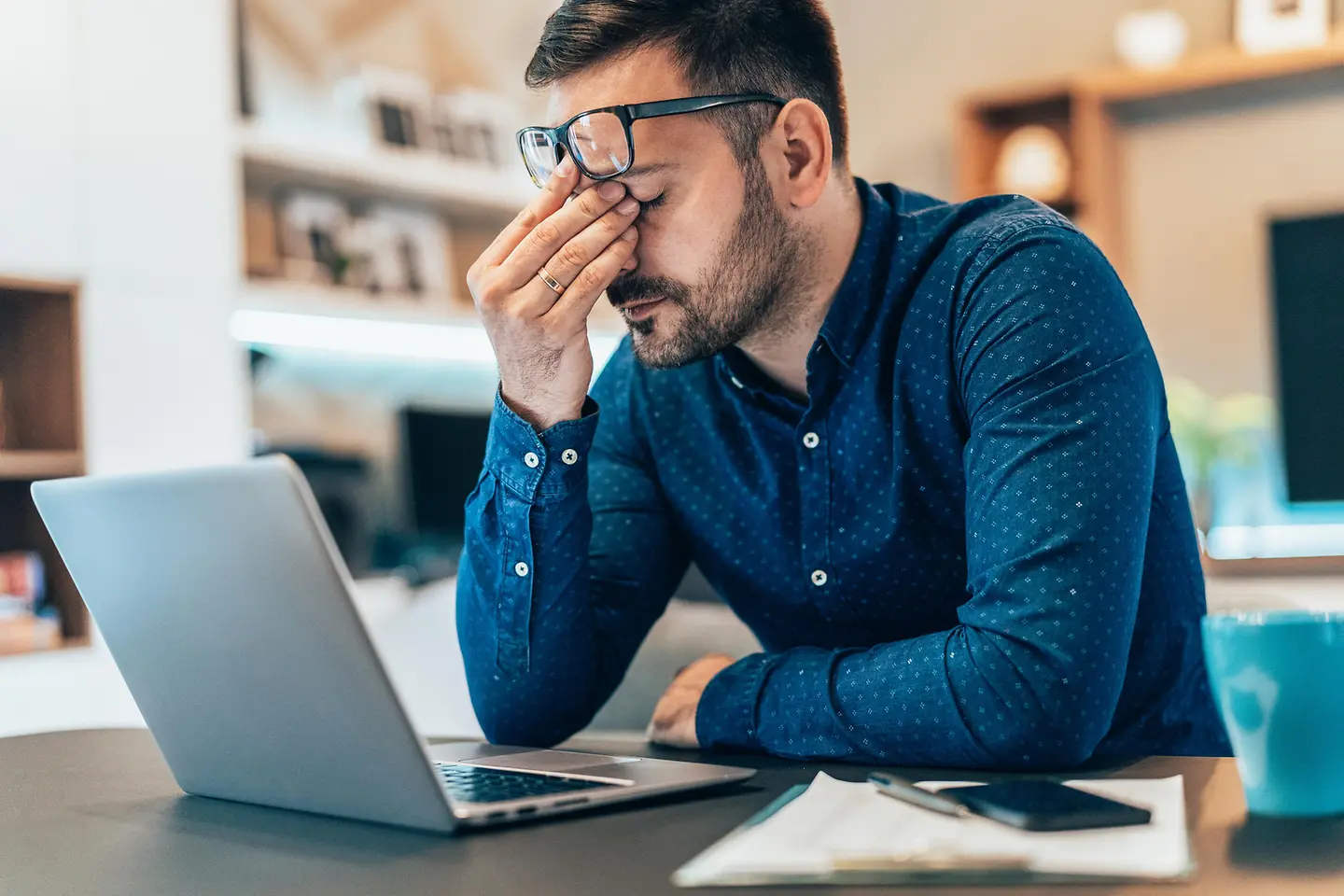 Ein gestresst wirkender Mann sitzt am Laptop und reibt sich die Augen. 