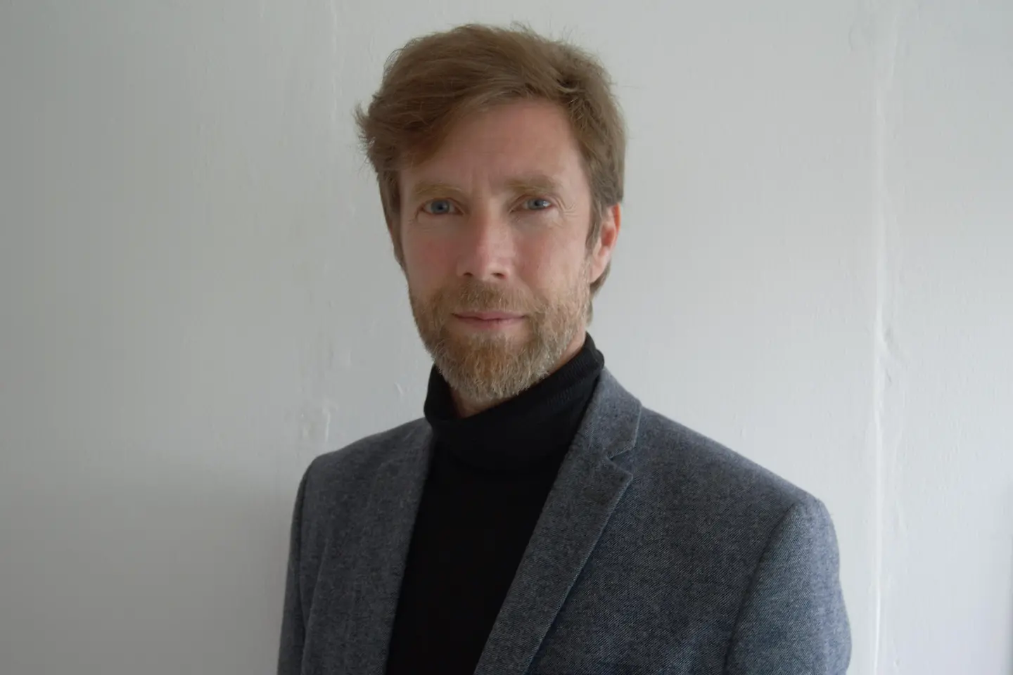 Ein Mann mit Bart, Sakko und Rollkragenpullover schaut in die Kamera.