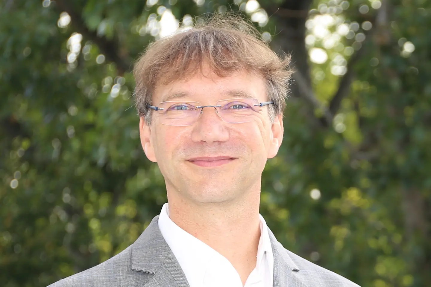 Ein Mann mit Brille und Anzug schaut in die Kamera.