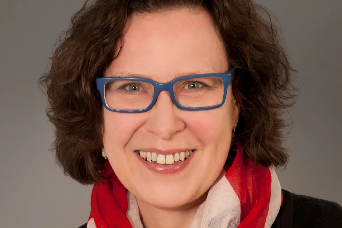 Eine Frau mit Brille und Schal lächelt in die Kamera.