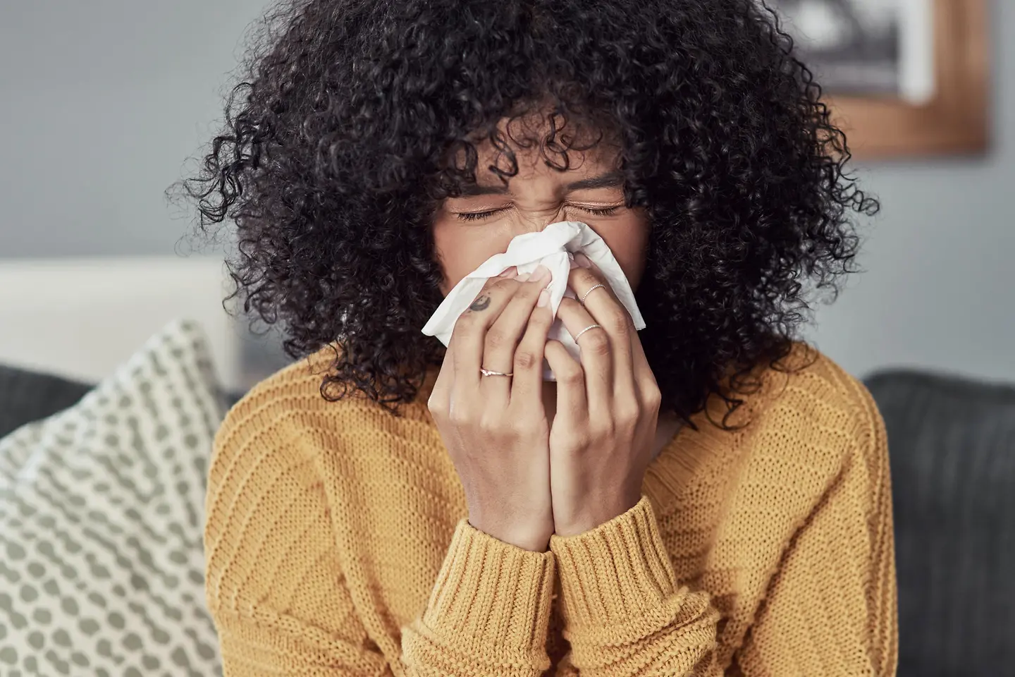 Dunkelhäutige junge Frau mit schwarzer Lockenmähne niest in ein Taschentuch.