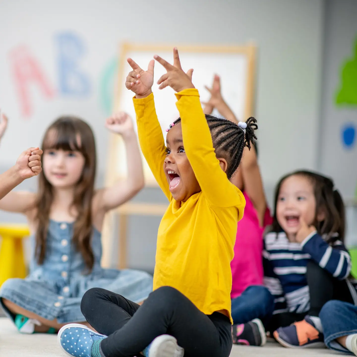 Kinder sitzen im Kindergarten auf dem Fußboden und heben die Hände in die Luft