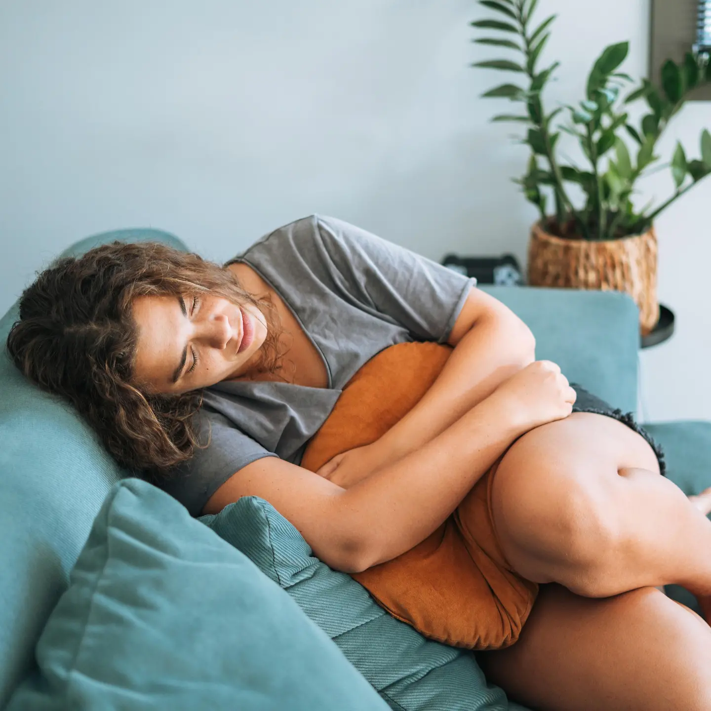 Frau liegt vor Schmerzen gekrümmt auf dem Sofa und hält sich beide Hände an den Bauch.