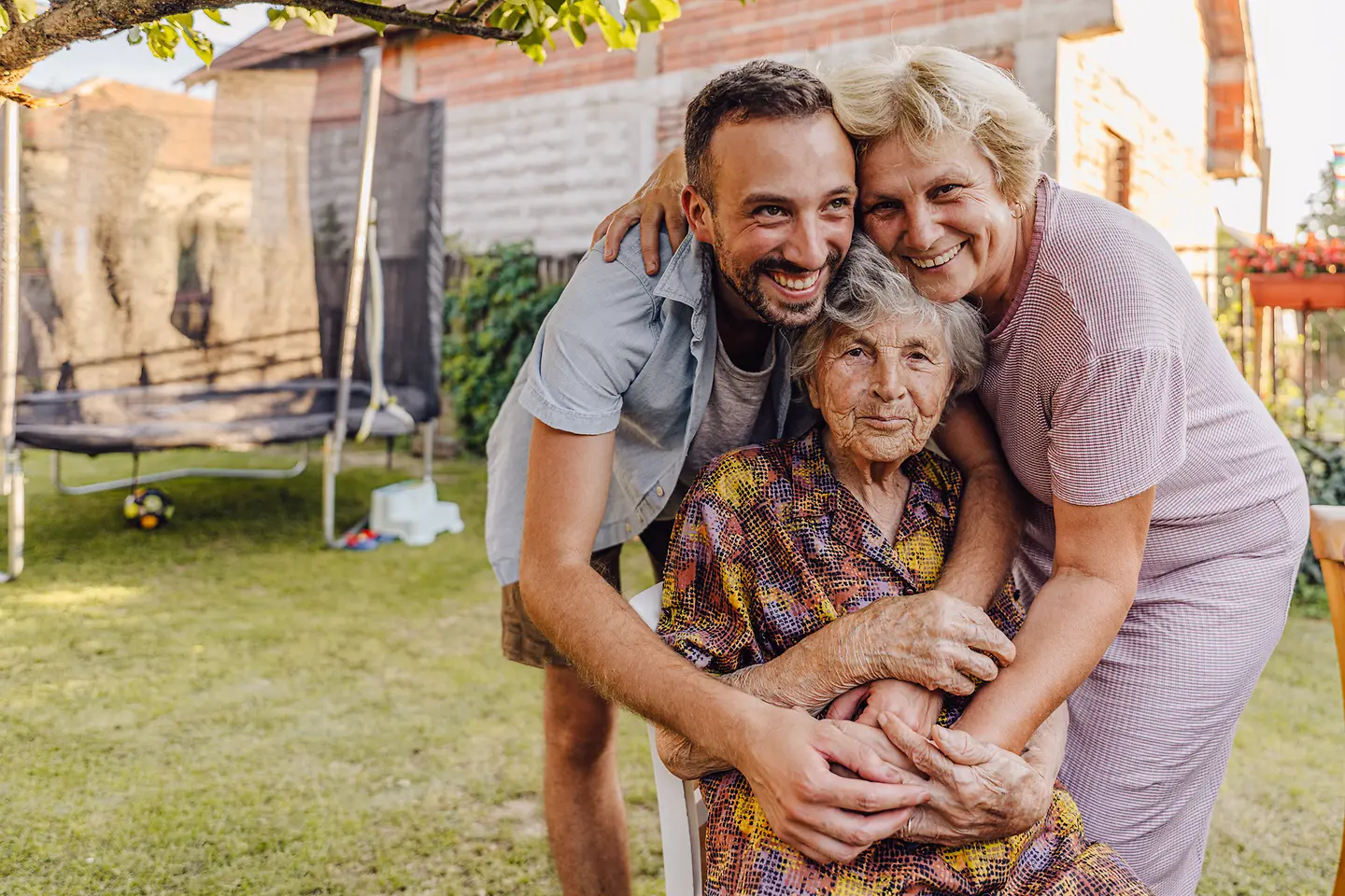 Ein Mann, eine sehr alte Dame und eine ältere Frau umarmen sich