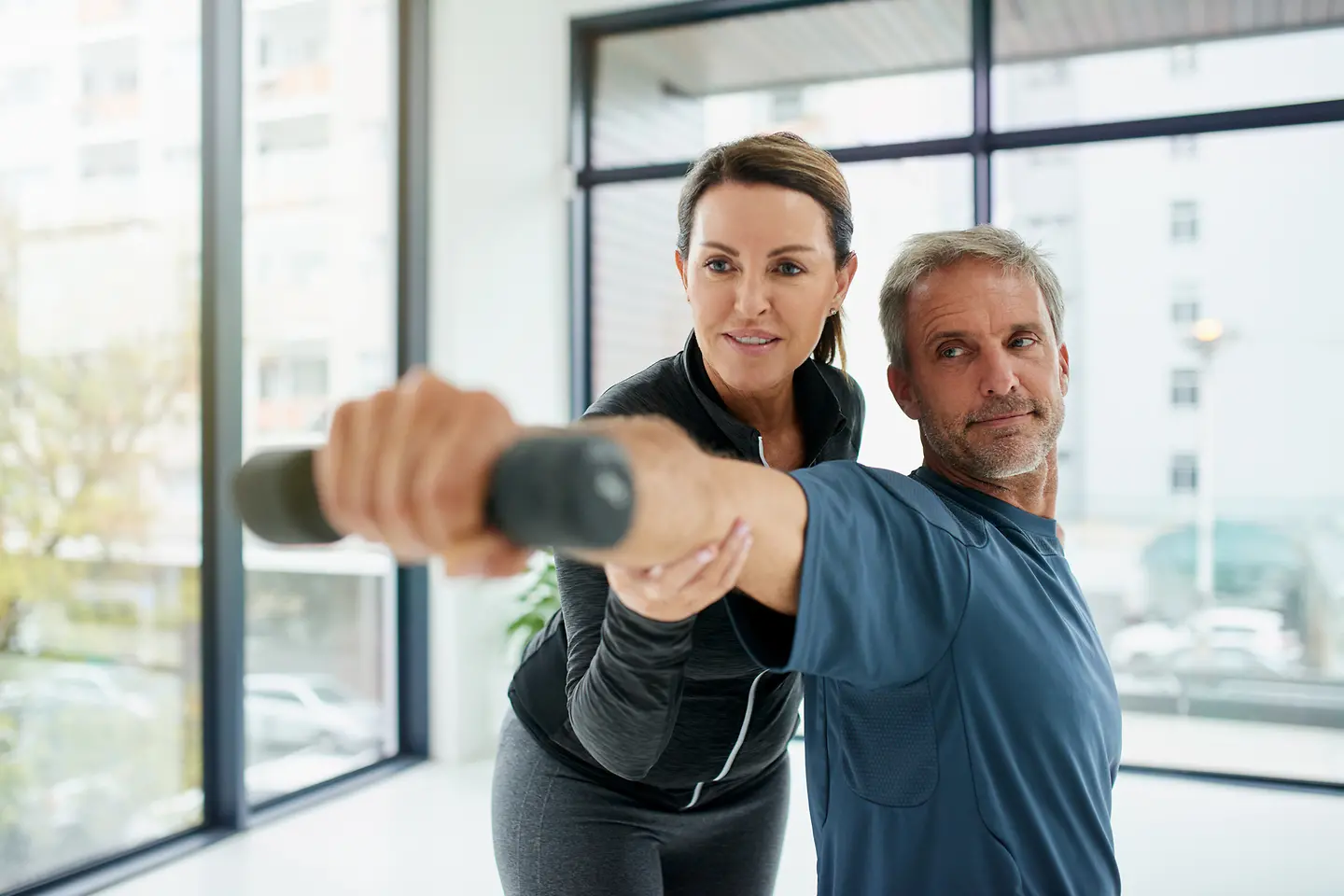 Eine Frau im Trainingsanzug gibt einem Mann Anleitung zur Physiotherapie