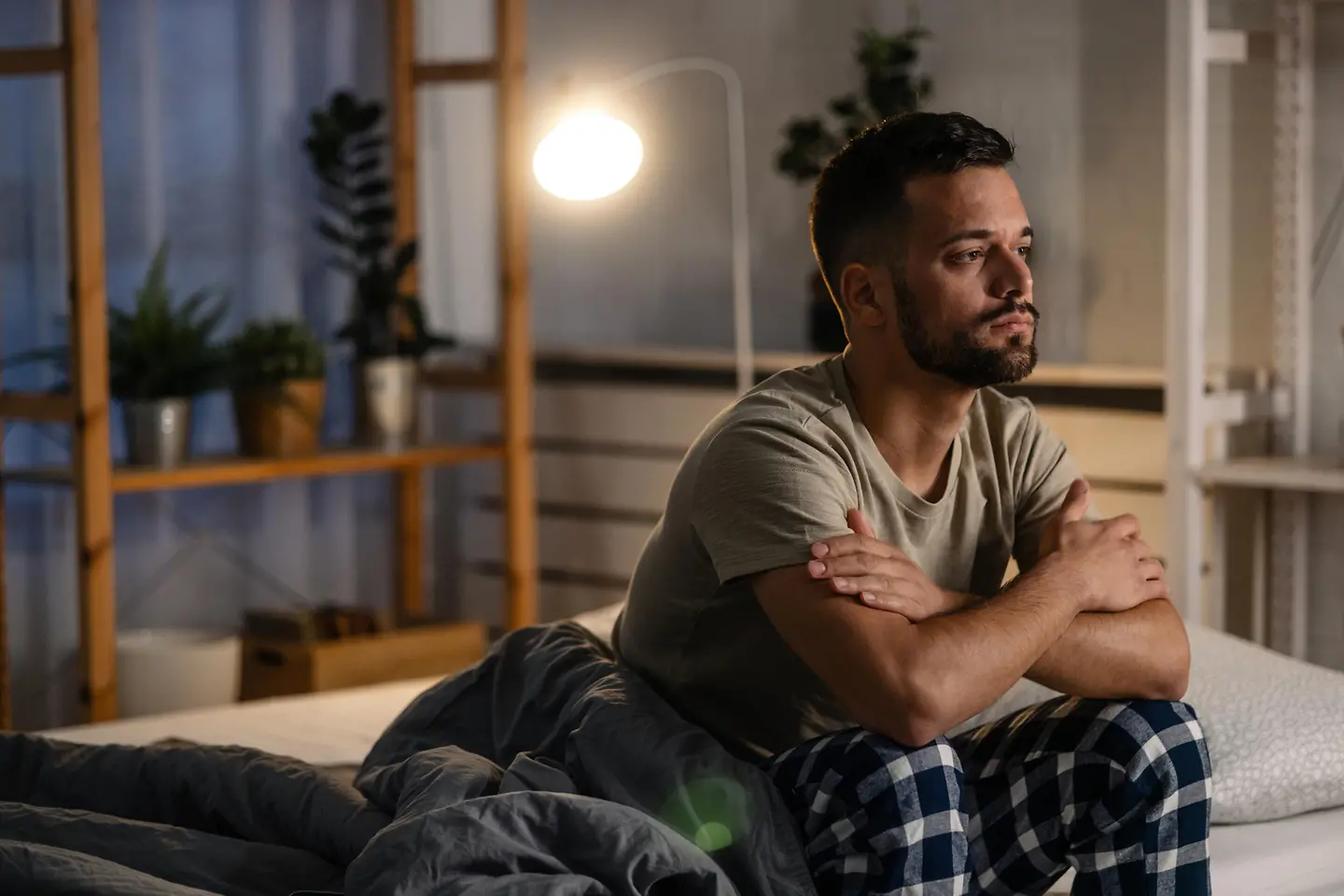 Junger Mann sitzt aufrecht in seinem Bett und kann nicht schlafen