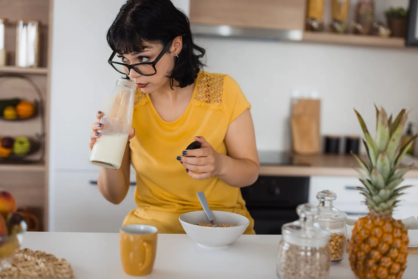 Eine Frau steht in der Küche und riecht an einer Flasche Milch.