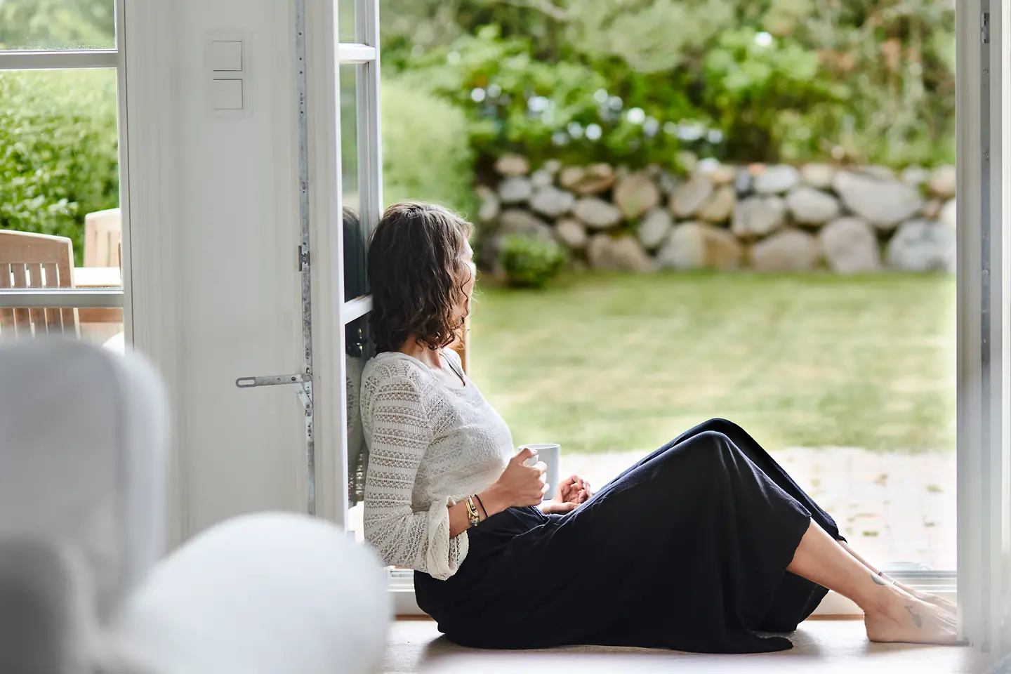 Frau sitzt in der Terrassentür und schaut in den Garten