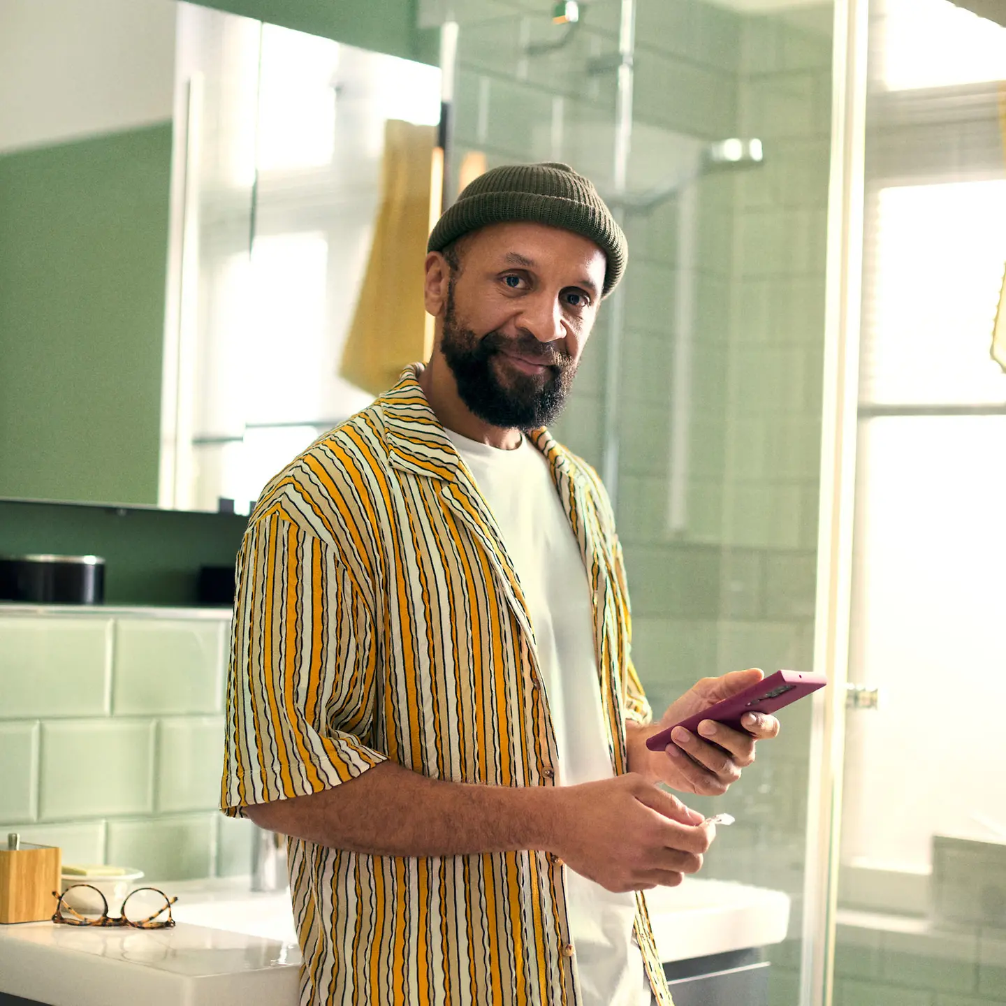 A man stands in the bathroom holding his smartphone and a medicine
