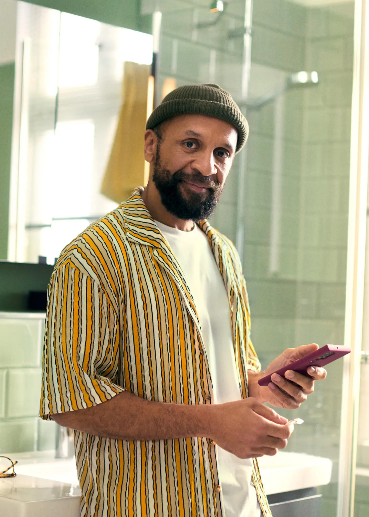 A man stands in the bathroom holding his smartphone and a medicine