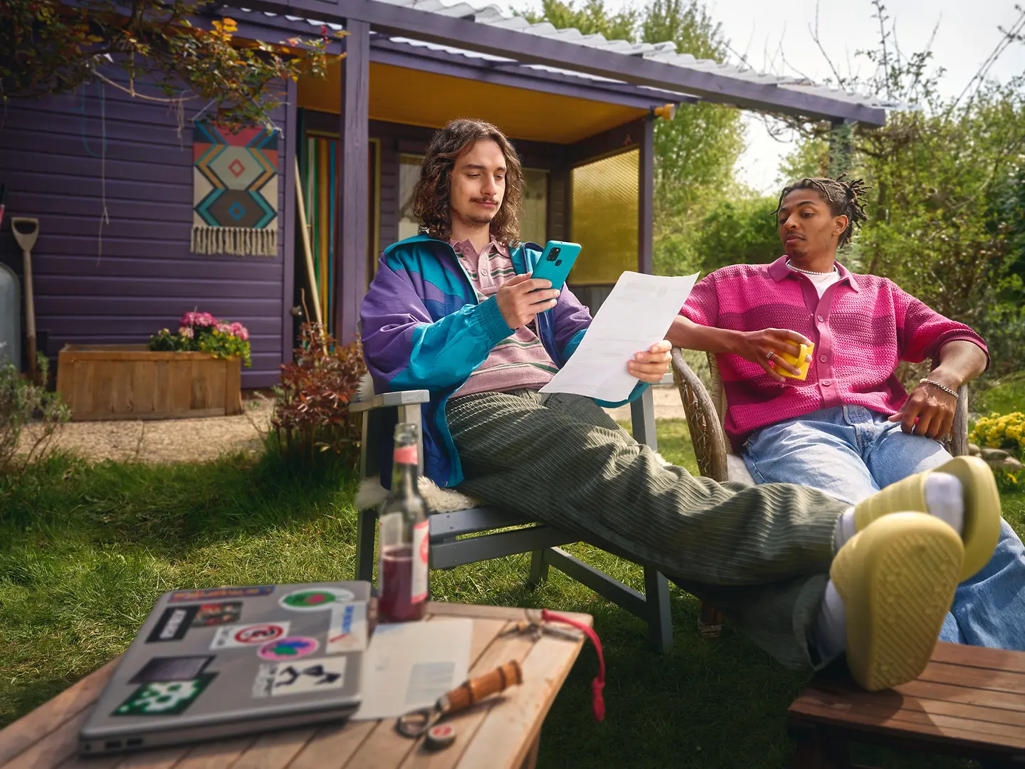 Zwei junge Männer sitzen im Kleingarten und schauen sich eine Rechnung auf Papier an
