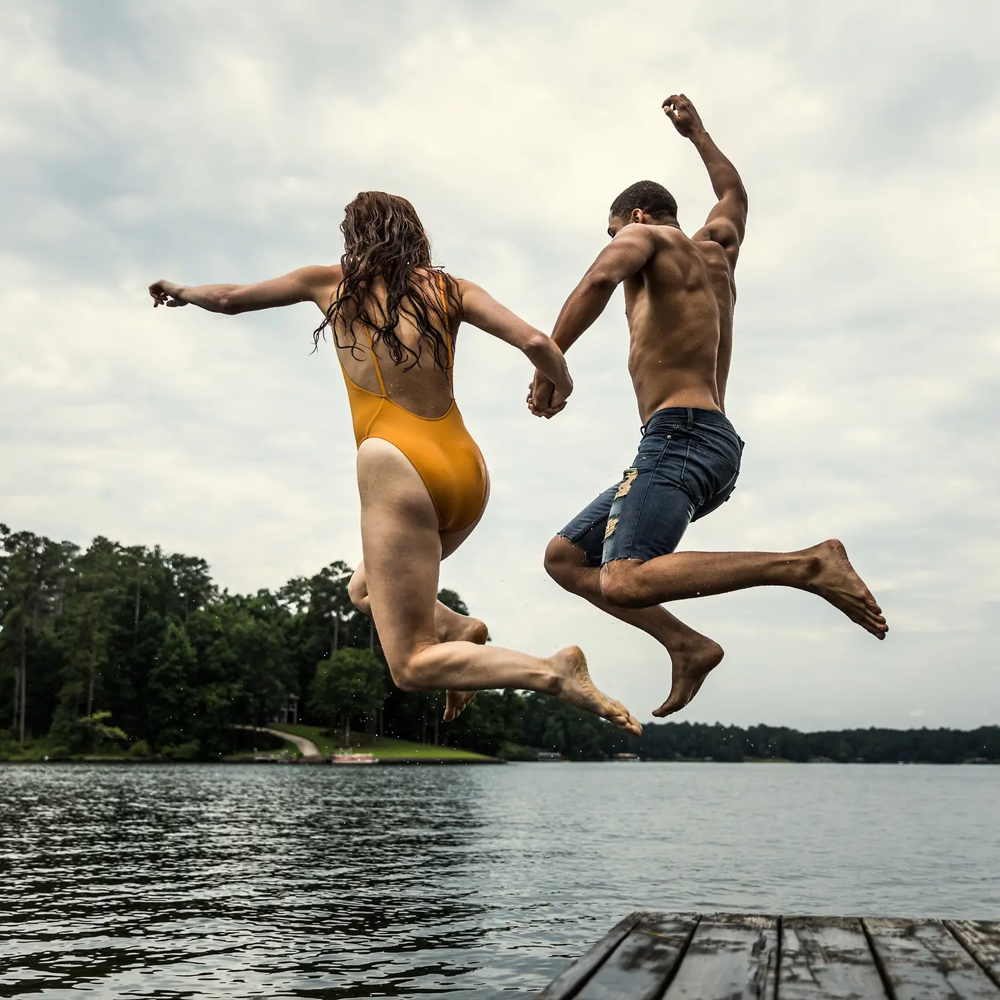 Junges Paar springt von einem Steg in einen See