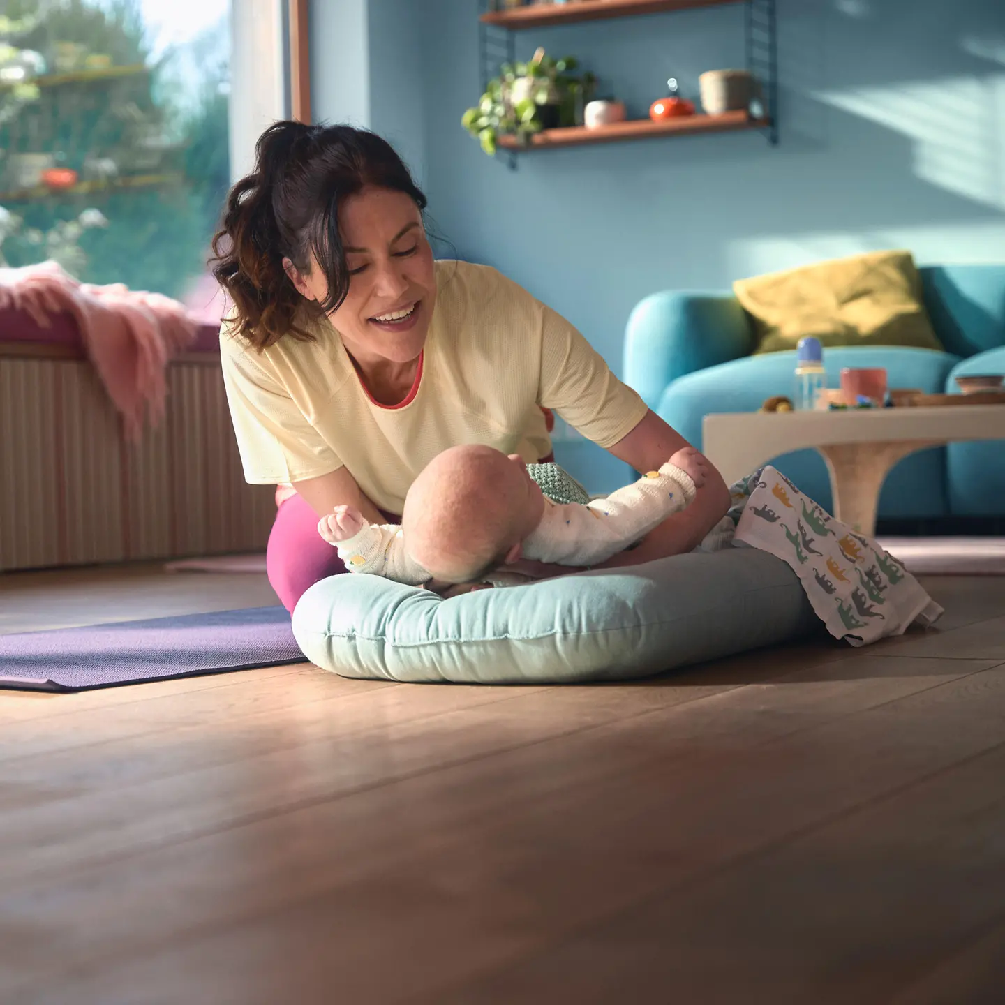 Eine Frau sitzt im Wohnzimmer und spielt mit ihrem Neugeborenen