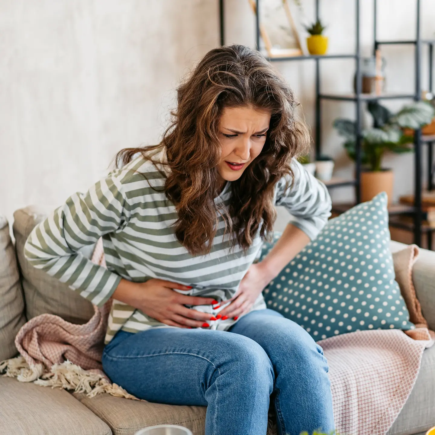 Frau sitzt nach vorne gebeugt mit Bauchschmerzen auf Sofa